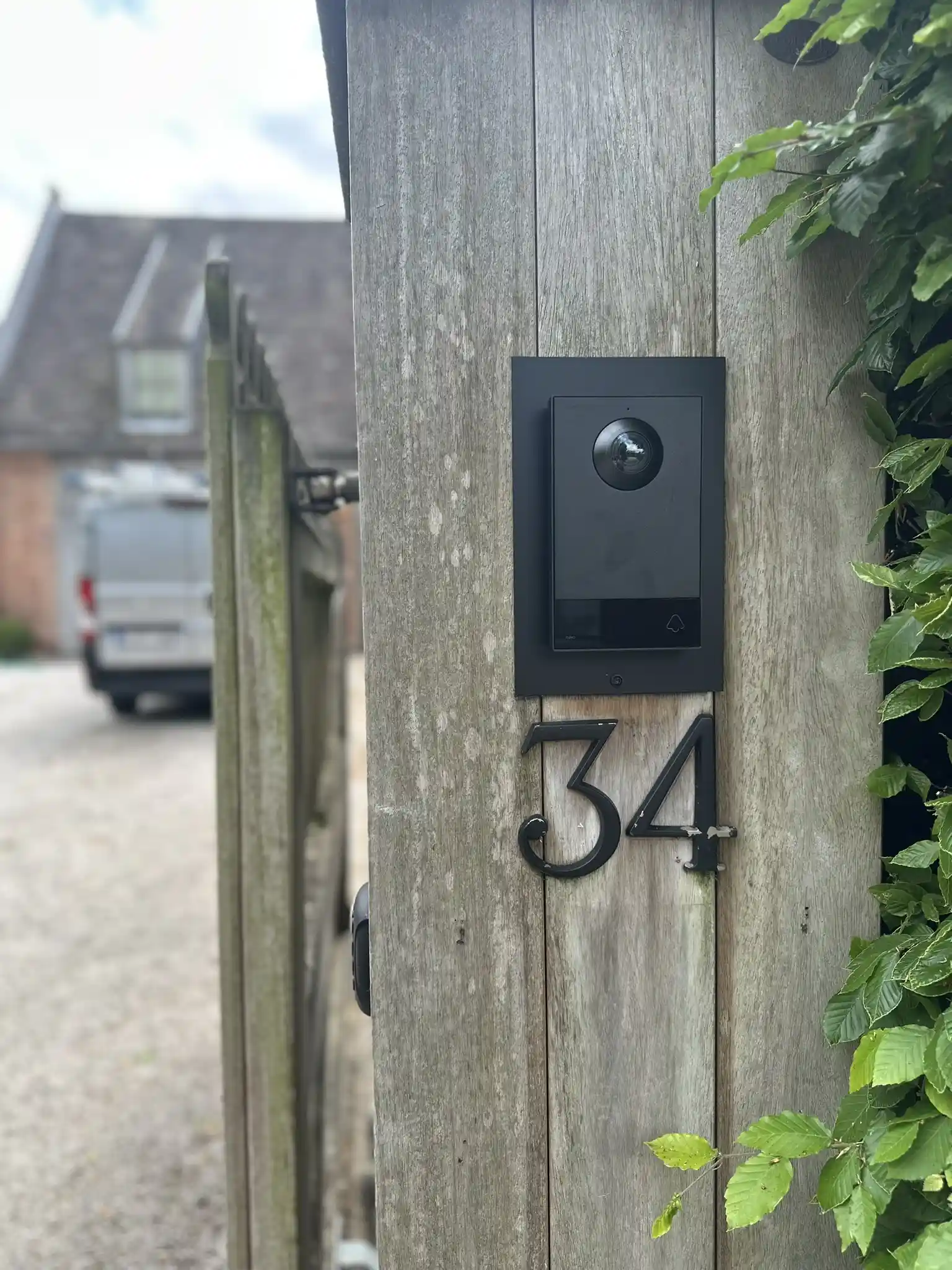Videofoon met camera bevestigd op houten hek met huisnummer, geplaatst door Bram Security in Dentergem.